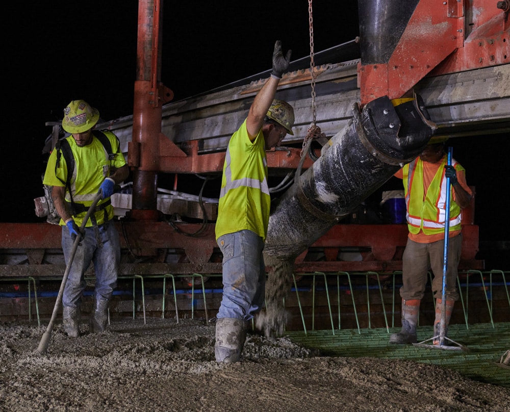 workers pouring concrete over rebar framing 